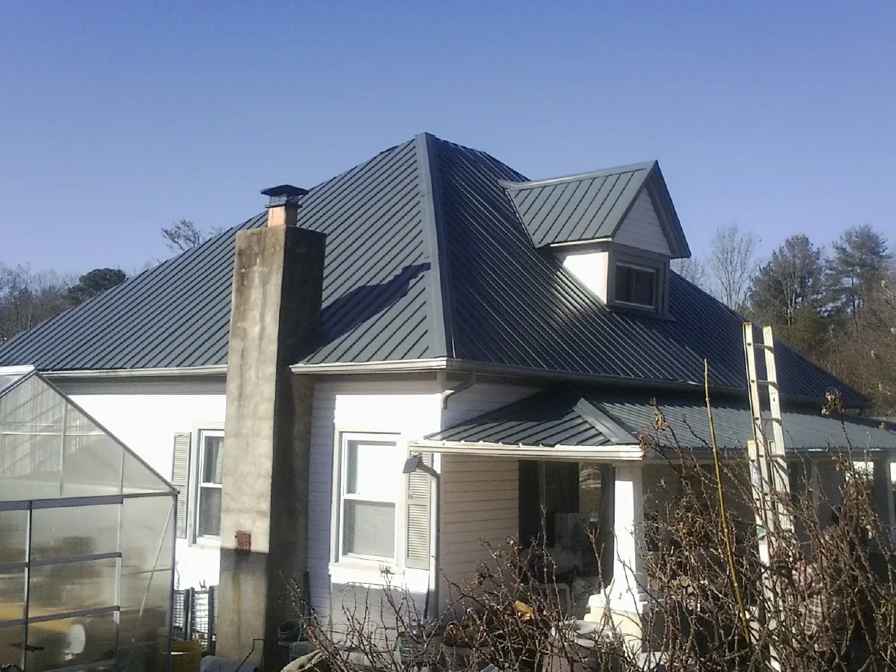 Dark blue standing seam metal roof on a white farmhouse with dormer — Slate & Tile Roof Repair by Roofing Brothers in Karval