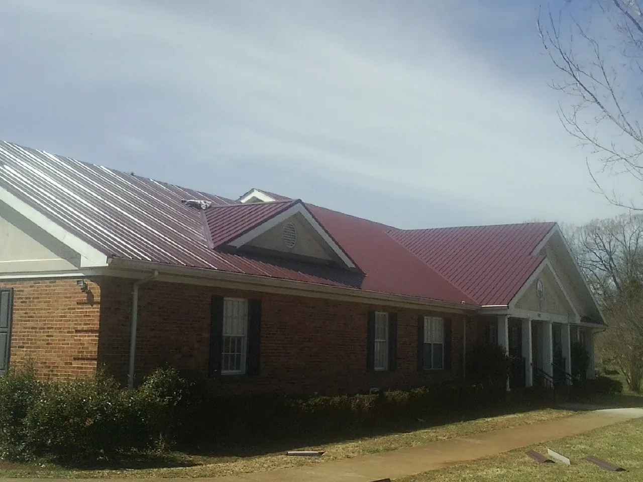 Red metal roof with gabled entries on a long brick building, from a Hail Damage Roof Repair job in Karval