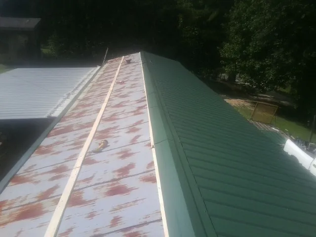 Old rusted panels beside newly installed green metal roofing — Wind Damage Roof Repair by Roofing Brothers in Karval