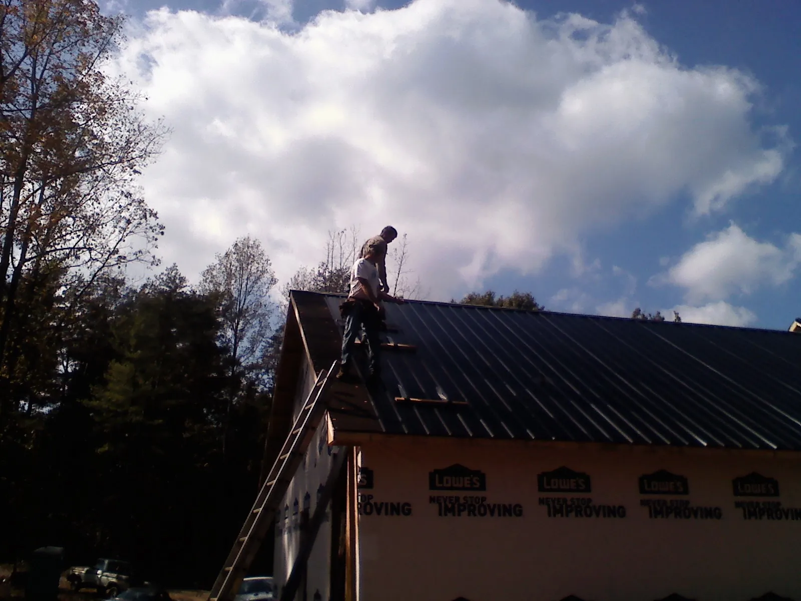 Roofer fastening dark metal panels high against a cloudy sky, from a Roof Inspection job in Karval